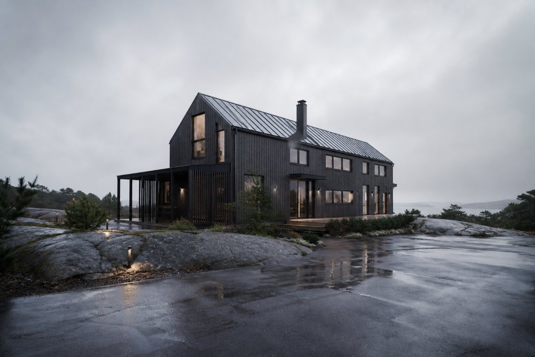 Exempelbild: Nybyggd villa i motljus en regnig eftermiddag. Vidvinkel, kameran lågt, blöt granit och våt asfalt i förgrunden, havsdis bakom taket. Kall färgtemperatur, inga personer i bild.